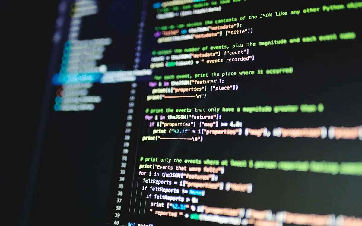 Close up of a monitor showing lines of colorful code on a dark background.