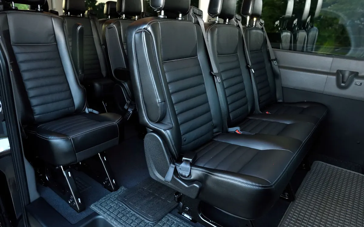 Rows of black leather passenger seats with seat belts inside a long passenger van, seen through the open sliding door.